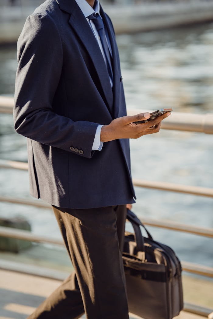 why-choose-us Man in business attire multitasks with phone and bag by a waterfront.