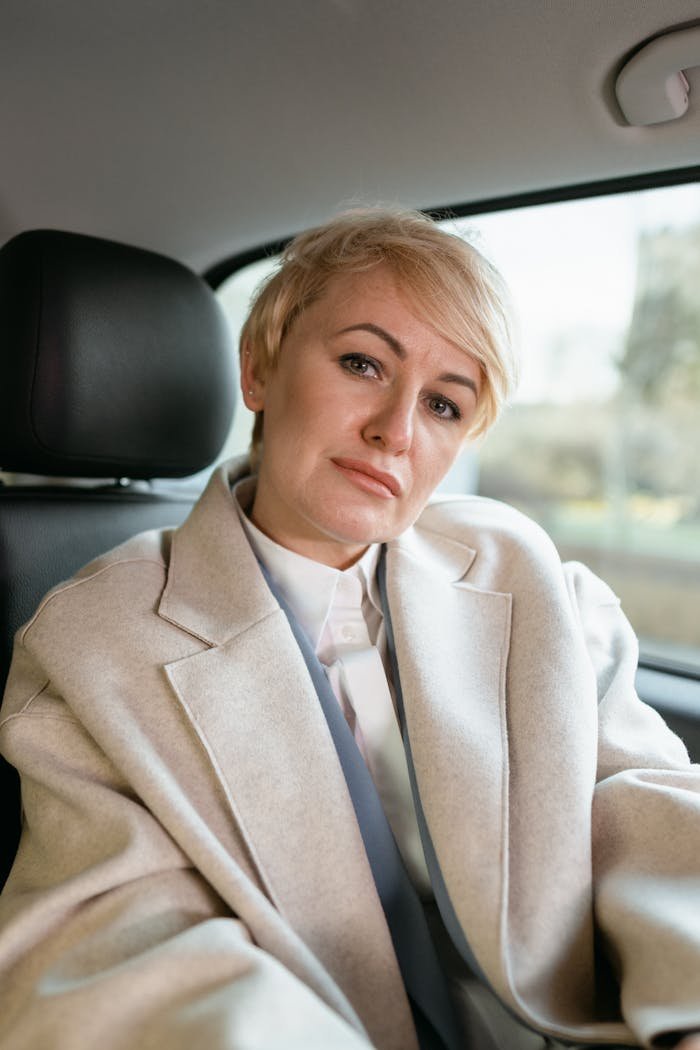 about-us A serious businesswoman with blond hair sitting inside a car, looking professional.
